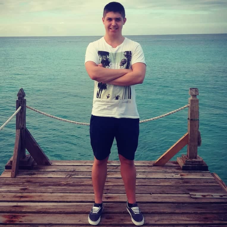 Mladý muž stojí na molu u moře, usmívá se.