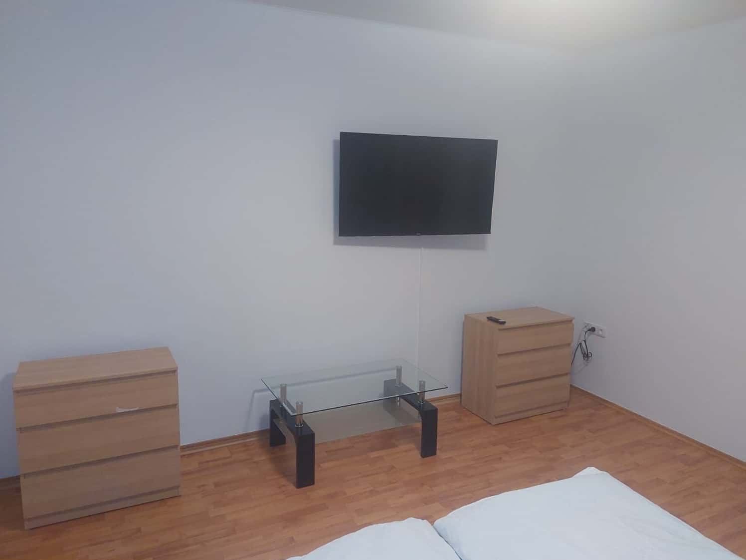 Moderní televizní sestava s nábytkem a plochou obrazovkou Televize na zdi s dvěma dřevěnými skřínkami a konferenčním stolkem v minimalistickém interiéru.