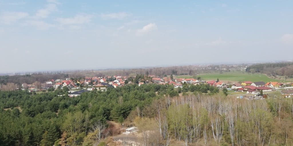 Výhled na Zvěřínek s lesy a vesnicí v pozadí.