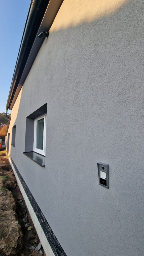 Moderní kamerový systém na bílé zdi domu s dveřním videotelefonem.
