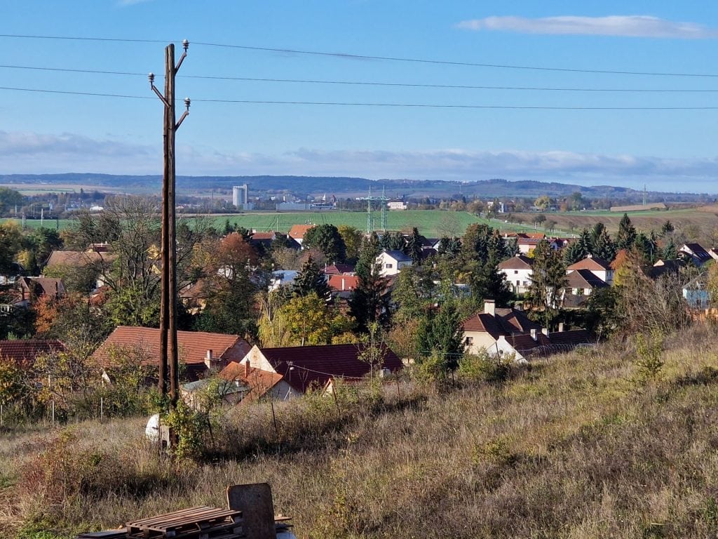 Klučov - panorama vesnice s domy, stromy a polemi pod modrou oblohou.