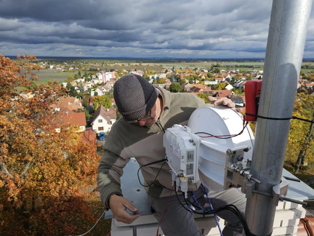Anténa a technik instalující Wi-Fi zařízení na střechu budovy.